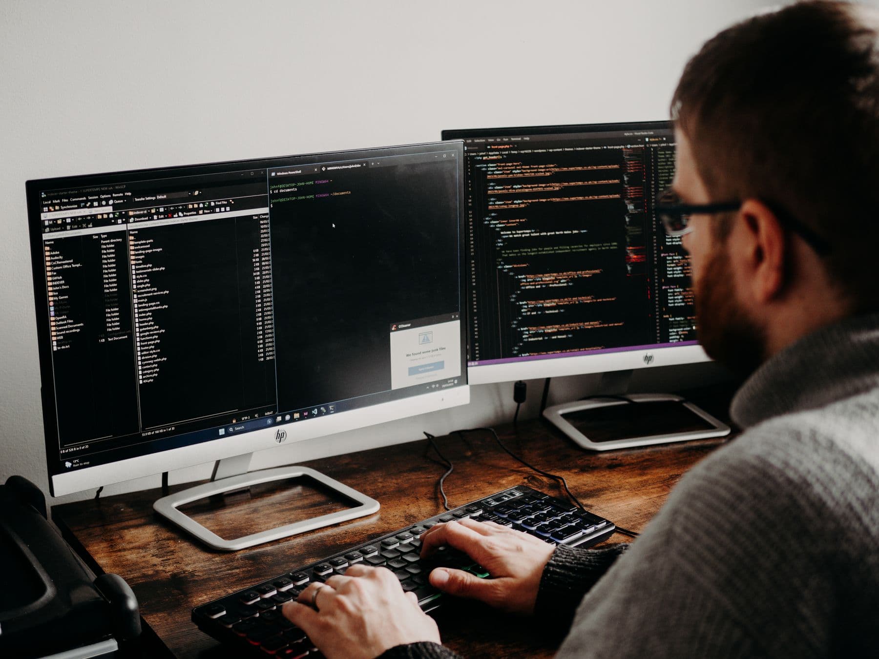 Software developer typing code on dual monitors